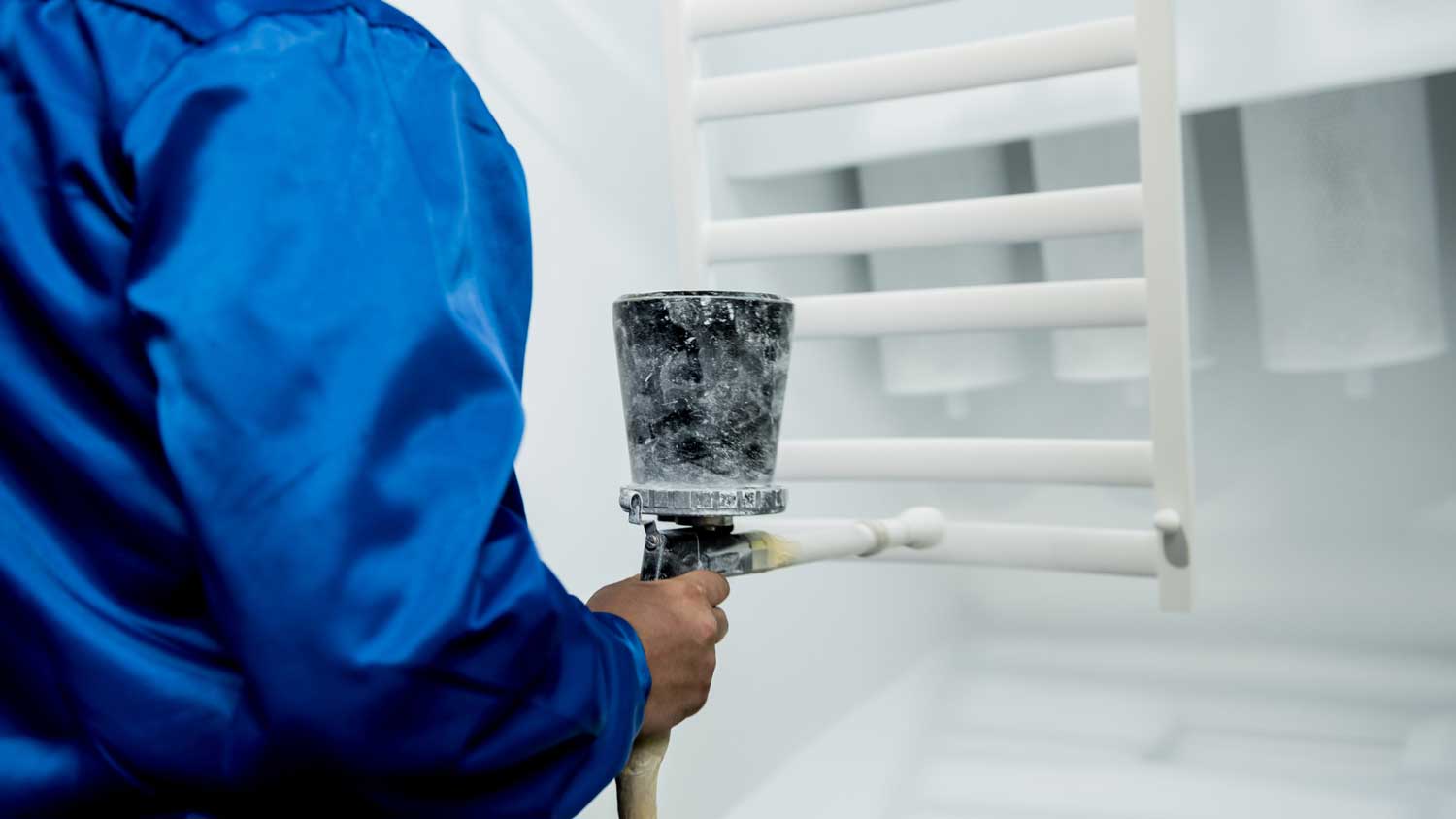 Worker performing powder coating of metal details at factory