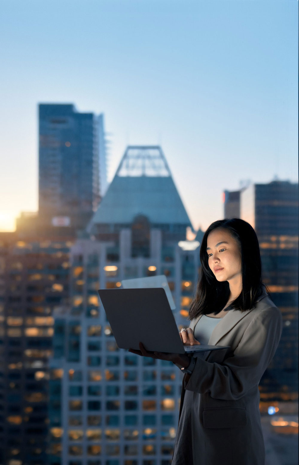 Young Asian business woman executive holding laptop standing at night office window